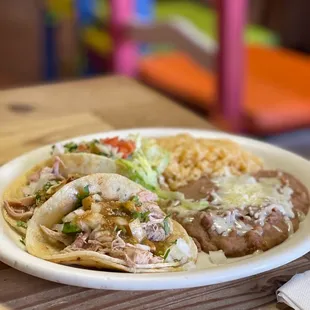 2 tacos filled with chicken, with a side of rice and beans and a little salad