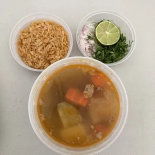 Caldo de Pollo O Res soup, Mexican Rice, container of red onion, jalapeños, cilantro, lime wedges