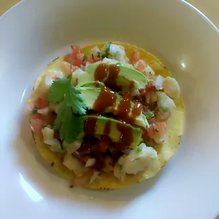 Ceviche with tilapia fish, a round corn chip on bottom and garnish with avcado and salsa valentina.