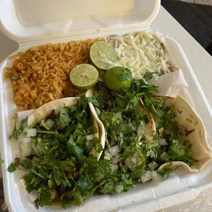 3 barbacoa tacos buried under lots of cilantro and onion with rice and beans.