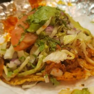 Al pastor tostada is piled high, side view.