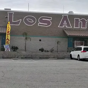 The restaurant is located at the front left corner of a big building that is a flea market inside.