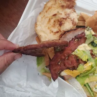 a person holding a sandwich with bacon and lettuce