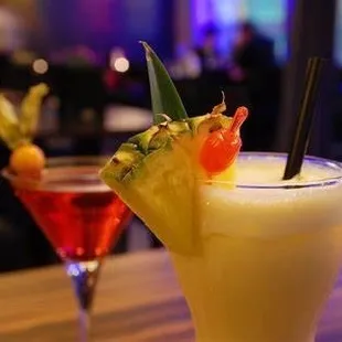 Cosmopolitan with a melon ball garnish and a pineapple rum with pineapple and cherry garnish