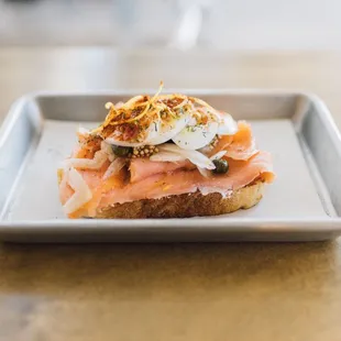 Salmon toast topped with boiled egg. capers, fennel, pickled mustard seeds and lemon zest.