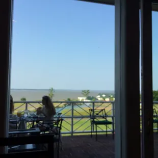 a woman sitting at a table on a balcony overlooking the ocean