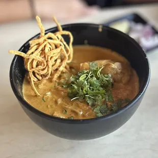 Khao Soi: egg noodles served w/chicken in coconut curry sauce, garnished w/sliced red onion, lime &amp; pickled mustard greens | $15