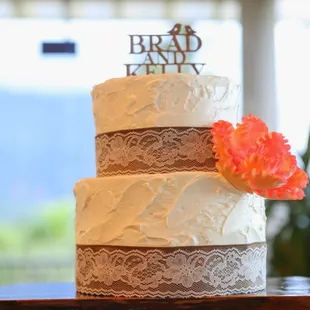 Rustic/vintage two-tier cake with lace-burlap trim and a coral sugar flower to match the wedding colors