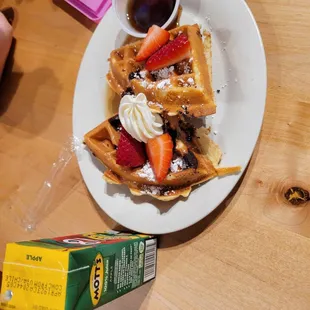 a plate of waffles with strawberries and syrup