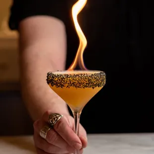 a woman holding a cocktail glass with a fire in it