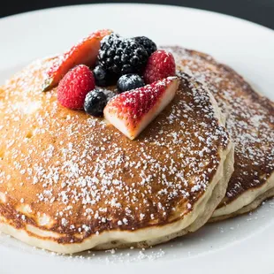 a stack of pancakes topped with berries and powdered sugar