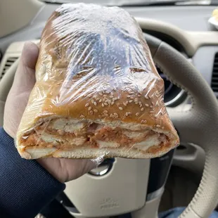 a hand holding a sandwich wrapped in plastic