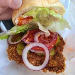 a hand holding a sandwich with lettuce, tomato, onion, and lettuce