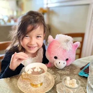 a little girl sitting at a table with a cup of hot chocolate