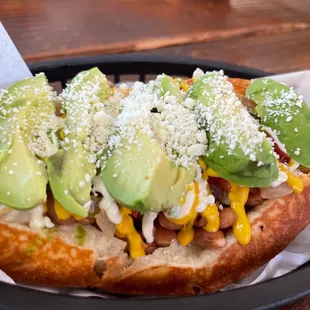 a hot dog topped with avocado and cheese