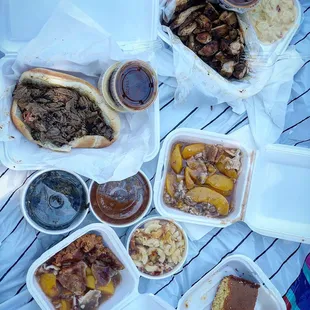 L to R : Beef Brisket Sandwich, Pulled Pork Dinner, Collard Greens, Baked Beans, Macaroni and Cheese, Slice of Peach Cobbler, Cornbread