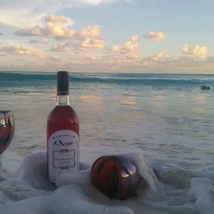 a bottle of wine and two wine glasses on the beach