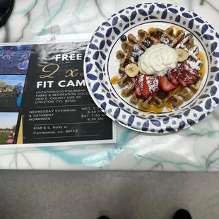 a plate of waffles with fruit and whipped cream