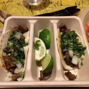 three tacos in a tray with lime wedges