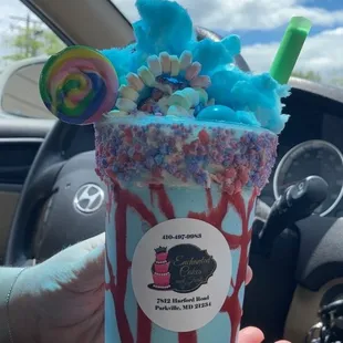 A cotton candy milkshake with cotton candy crumbles, lollipop and cotton candy on top.