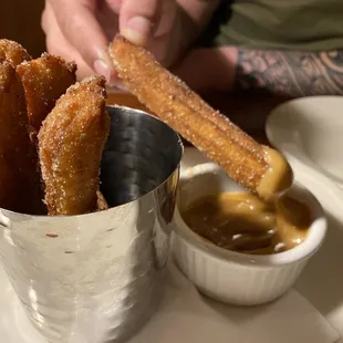 a person dipping churros into a cup