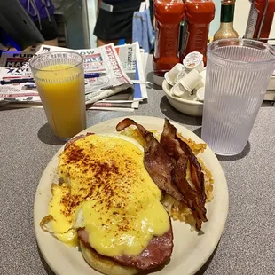 Classic Eggs Benedict with hash brown, a side of bacon and a glass of orange juice.