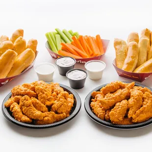 two plates of chicken wings, carrots, celery sticks, and dips