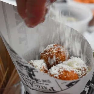 a person sprinkling sugar on a donut