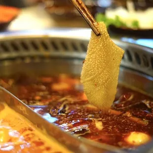 a person dipping a piece of food into a hot pot
