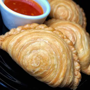 three pastries on a plate with dipping sauce