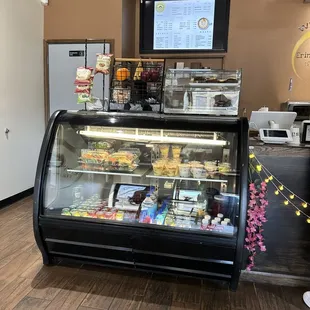 A warm welcoming shop featuring a pastry cabinet with a digital menu above