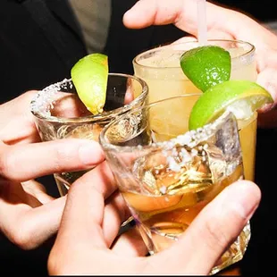 a close up of a person's hands holding two glasses of alcohol