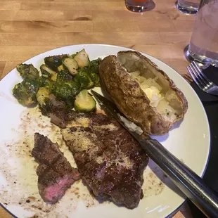 Ribeye steak cooked medium with baked potato and Brussel sprouts