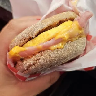 a hand holding a sandwich with cheese and ham