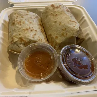 two burritos in a styrofoam container with condiments