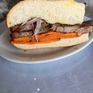 a steak sandwich with carrots and onions