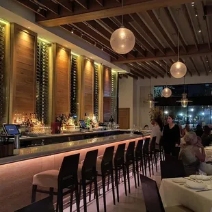 a restaurant with a long bar with wine bottles on the wall