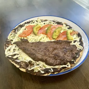 Tlayudas istmenas dish - a large toasted tortilla with beans, Oaxaca cheese, tomato, avocado, and a pork skin.