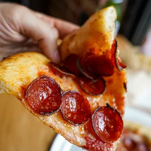 a hand holding a slice of pepperoni pizza