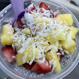 a hand holding a plastic cup filled with strawberries, pineapples, and strawberries