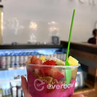 a hand holding a cup of fruit and yogurt