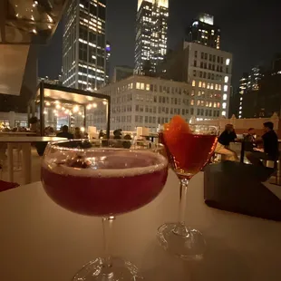 two cocktails on a table in front of a cityscape