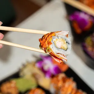 a person holding chopsticks over a plate of sushi