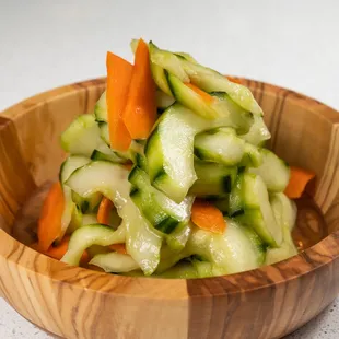 a wooden bowl filled with cucumbers and carrots