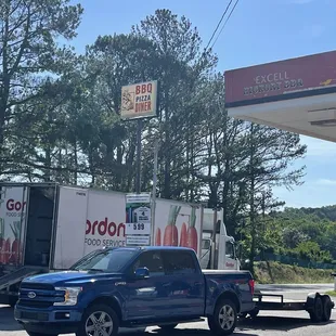 ows a blue truck parked in front of a gas station