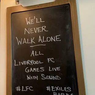 a blackboard with a sign that says we'll never walk alone all liverpool fc games live with sound