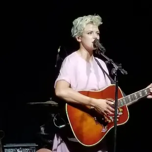 a woman playing a guitar and singing into a microphone