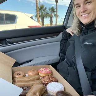 a woman sitting in a car with a box of doughnuts