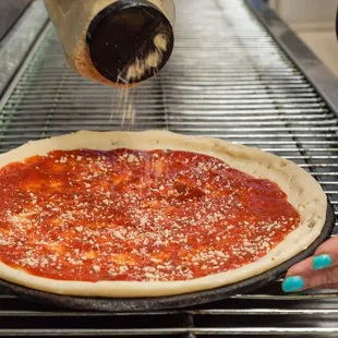 a person sprinkling cheese on a pizza