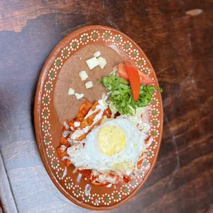 Red chili chilaquiles with an egg on top beans and garnish